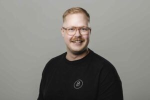 Ein Mann mit schwarzem Shirt und Brille laechelt in die Kamera.